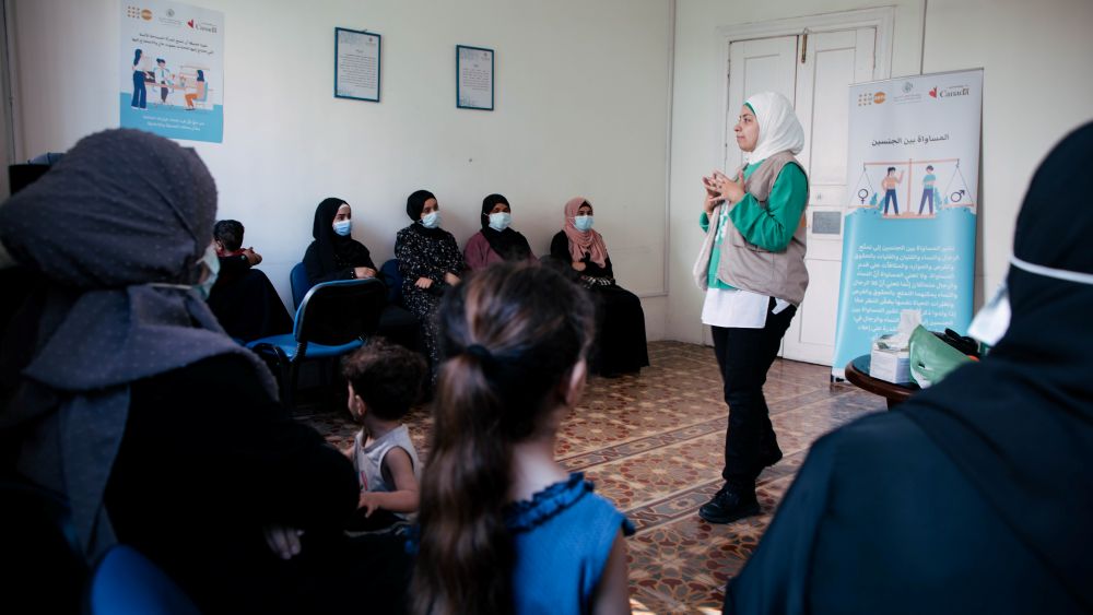 مجموعة من النساء يحضرن جلسة دعم نفسي اجتماعي بينما تقف المدربة في وسطهن.