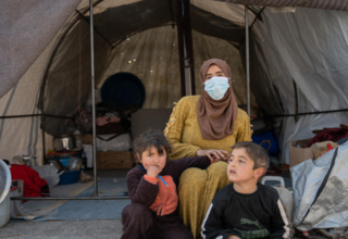   Um Abdul Hamid sits with her children in front of their tent in Al-Hamam makeshift camp in Jinderis