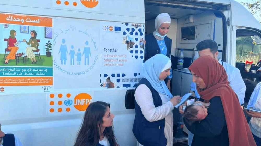 A mother holds her baby surrounded by health service providers in front of a UNFPA-supported mobile health clinic