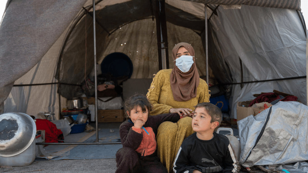   Um Abdul Hamid sits with her children in front of their tent in Al-Hamam makeshift camp in Jinderis